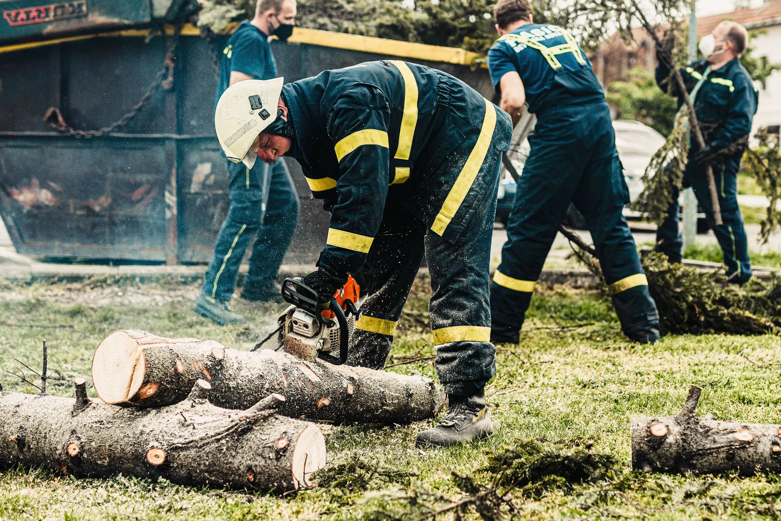 Firefighters in protective gear using a chainsaw to clear fallen trees outdoors. Teamwork in action. Tree service metrics: monthly tracking without the noise