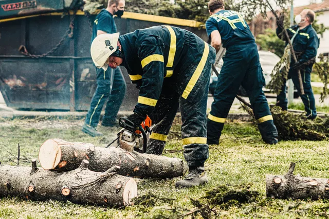 Firefighters in protective gear using a chainsaw to clear fallen trees outdoors. Teamwork in action. Tree service metrics: monthly tracking without the noise